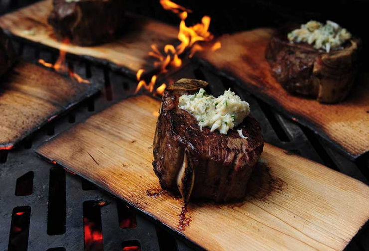Filet mignon steak cooking on wood grilling plank
